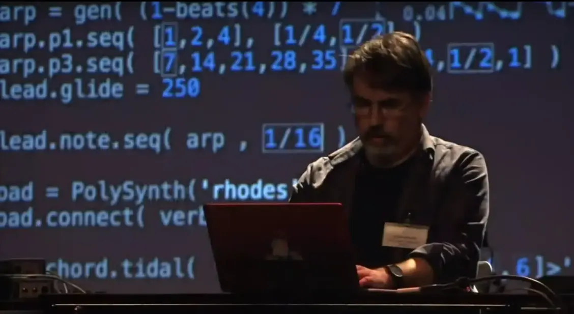 Me in front of a large screen projecting code from a performance, live coding on a laptop.